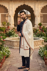 Side angle of a groom wearing an ecru beige Kashmiri men's wedding shawl with rust Sozni border detailing.