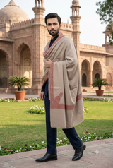 Pakistani model wearing a natural beige men's Kashmiri shawl with a terracotta-rust embroidered border over a navy sherwani in a palace garden