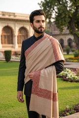 Handsome bearded model in a charcoal black bandhgala suit draped with a men's beige Kashmiri shawl featuring an embroidered rust border.