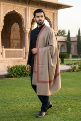 Young man wearing a men's fawn beige Kashmiri embroidered border stole layered over ethnic menswear in a palace courtyard.