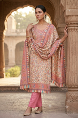 A woman models a traditional Indian salwar kameez suit set in a stone courtyard. The set features a beige kurta with a vibrant pink, orange, and blue floral print, a matching draped dupatta, and solid pink wide-leg pants.
