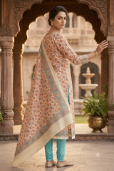 A woman models a traditional Indian salwar kameez suit in a courtyard with arches. The outfit features a beige kurta with a multicolor floral print, a matching printed dupatta with a solid beige border, and light teal pants.