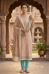 A woman models a traditional Indian salwar kameez suit in a courtyard with arches. The outfit features a beige kurta with a multicolor floral print, a matching beige dupatta with a green border, and teal leggings.