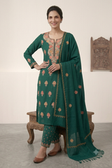 A woman models a traditional Indian salwar kameez suit in emerald green, featuring floral embroidery in pink and gold, paired with matching green trousers and a sheer green dupatta with gold borders.