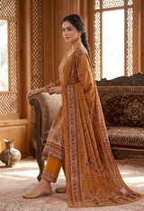 A woman models a traditional Indian salwar kameez suit in a warm brown and gold color palette, featuring a printed kurta, solid yellow trousers, and a matching dupatta, set against an ornate wooden interior background.