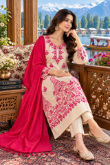 A woman models a traditional South Asian salwar kameez suit set. The set features a beige kurta with vibrant pink floral embroidery, matching beige trousers, and a bright pink dupatta draped over her shoulder.