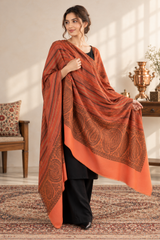 A woman models a large rust-orange shawl with intricate paisley and striped patterns, draped over her shoulders 
