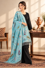 A woman models a light blue shawl with intricate multicolor paisley and floral patterns, draped over her shoulders. 