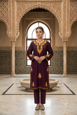 Pakistani model wearing a plum wine Kashmiri embroidered knee-length phiran kurta  in a royal palace courtyard.