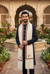 Pakistani male model in a royal palace garden wearing an ivory-beige Kashmiri embroidered men's shawl over a navy sherwani.