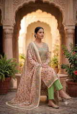 A woman seated in an ornate courtyard wearing a traditional Indian salwar kameez outfit. The outfit features a beige base with intricate multicolor floral embroidery, a matching embroidered dupatta, and light green trousers.