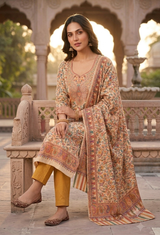 A woman models a traditional Indian salwar kameez suit set in an outdoor courtyard with stone arches. The set features a beige and orange printed kurta and dupatta with yellow trousers.