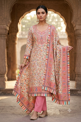 A woman models a traditional Indian salwar kameez suit set in an outdoor stone archway setting. The set features a beige kurta heavily embroidered with pink, orange, and green floral patterns, paired with solid pink trousers and a matching patterned dupatta.