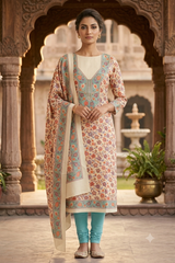 A woman stands in an ornate courtyard wearing a traditional Indian salwar kameez outfit. The outfit features a cream-colored kurta with a multicolor floral print, a matching printed dupatta, and teal leggings.