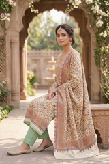 A woman models a traditional South Asian salwar kameez set in an outdoor courtyard with stone arches. The outfit features a beige and cream base with intricate multicolor floral prints and a matching patterned dupatta, paired with sage green pants.