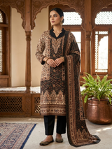 A woman models a traditional South Asian salwar kameez suit in a wooden architectural courtyard. The three-piece set features a black base with intricate beige and gold floral embroidery, paired with black trousers and a matching dupatta.