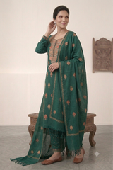 A woman models a traditional Indian outfit consisting of a dark green kurta with gold floral prints, matching green trousers, and a coordinating green dupatta with gold border detailing, set against an indoor neutral background.