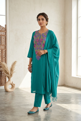A woman models a teal green kurta set with a matching dupatta and trousers. The kurta features a colorful purple and pink floral embroidered yoke.