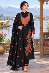 A woman models a black three-piece traditional outfit with orange-red floral embroidery, featuring a long kurta, matching pants, and a draped shawl, set against a scenic lake and mountain background.
