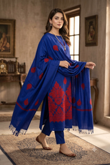 A woman models a royal blue three-piece salwar kameez suit with red printed motifs, featuring a matching dupatta draped over her shoulders in an indoor setting.